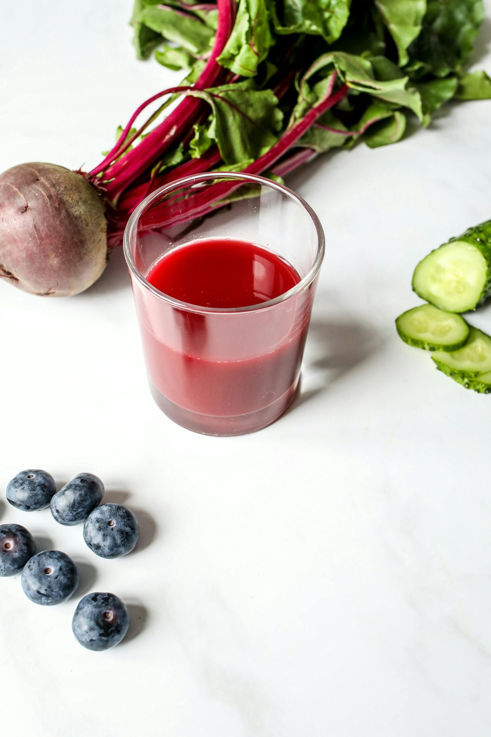 Refreshing beet juice with fresh blueberries, cucumber, and beetroot on a white background.
