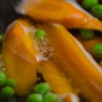 Close-up of carrots and peas boiling with bubbles in hot water, showcasing fresh vegetables.